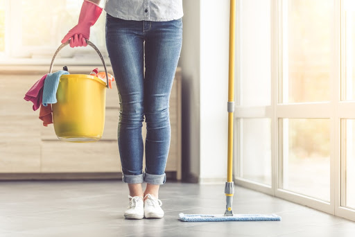 Mulher com balde amarelo e produtos de limpeza para pisos